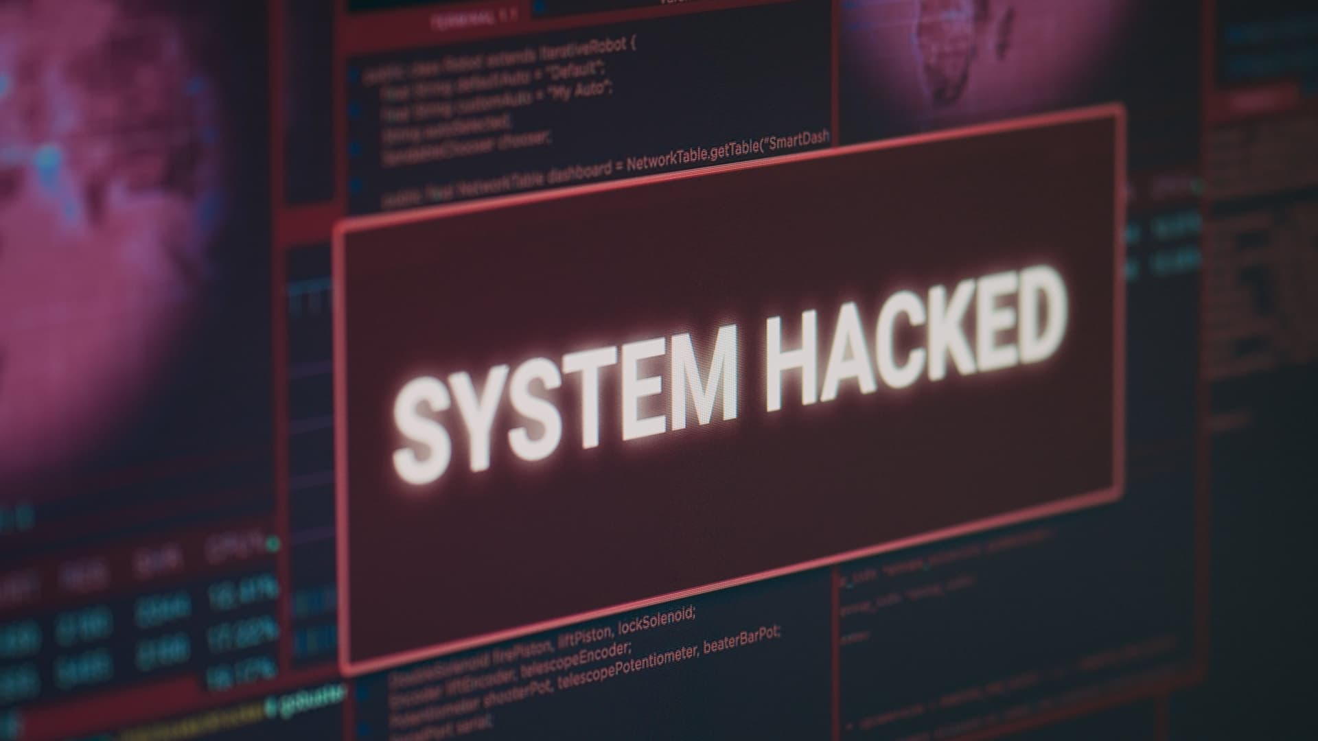 Skärm med varningstexten "System hacked" mot en bakgrund av kod och digitala gränssnitt.
