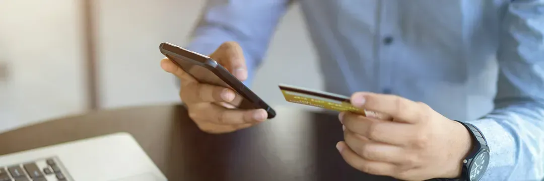 Man håller ett bankkort i ena handen och mobil i den andra – illustrerar processen kring kreditupplysning och hur det påverkar kreditvärdighet.