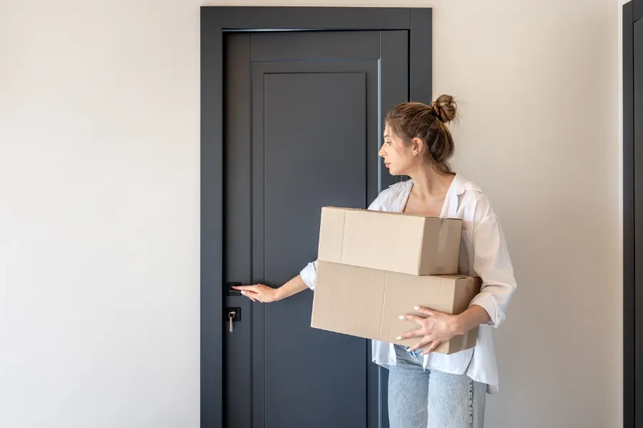 Kvinna som håller flyttkartonger och låser upp en dörr i en lägenhet, i samband med inflytt eller adressändring.