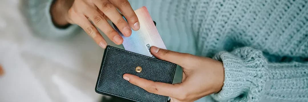 Person stoppar in ett färgglatt kort i en svart plånbok – illustrerar vikten av RFID-skydd för att förhindra skimming av betalkort.