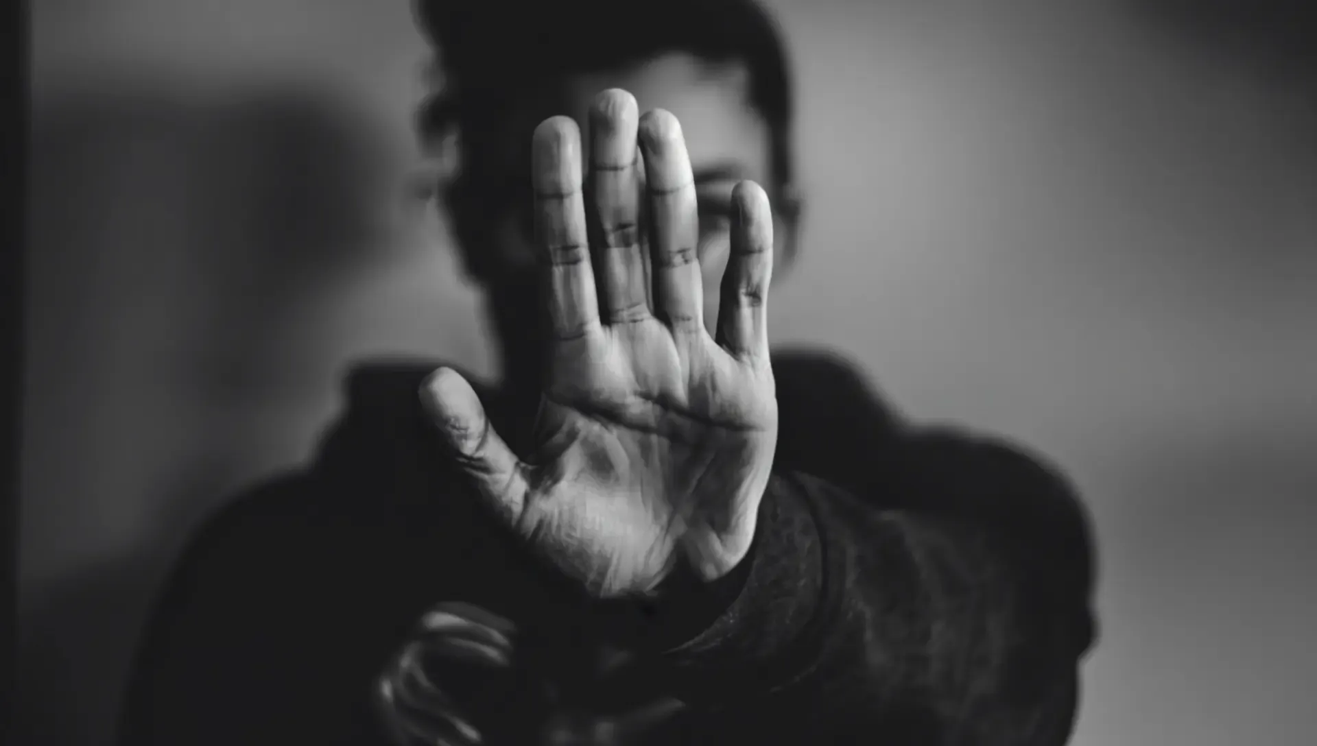 Person i svartvitt håller upp handen framför kameran för att dölja sitt ansikte – symboliserar skyddad identitet och rätten till anonymitet.