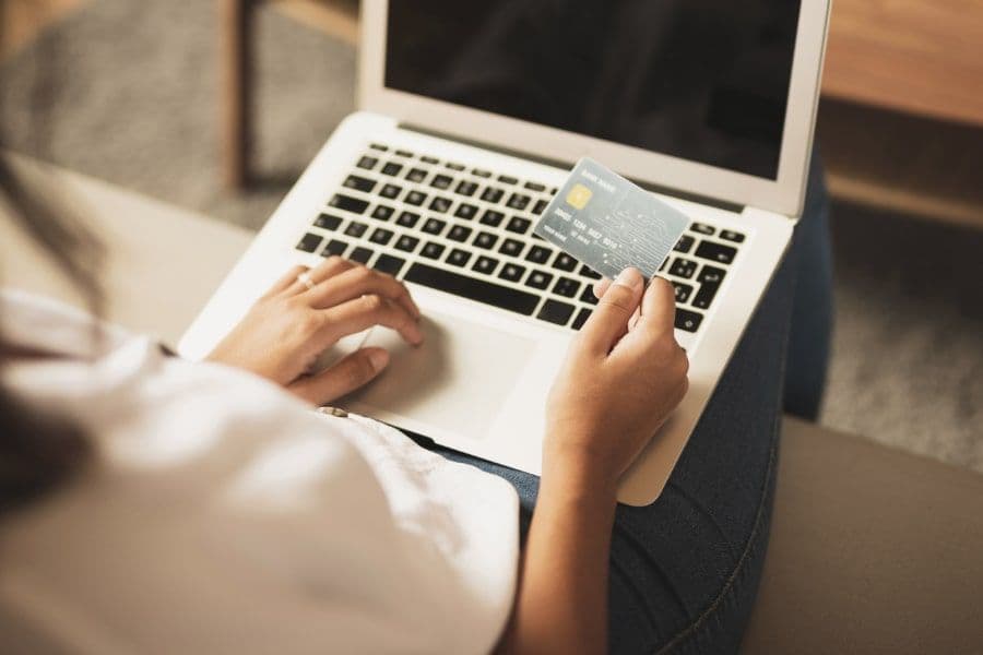 En person håller ett kreditkort i handen och använder en laptop för att göra en onlinebetalning.